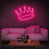 Pink crown LED neon sign glowing on the wall in a stylish living room with a white sofa and plants.