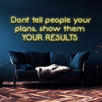 Yellow neon sign stating 'Don't tell people your plans, show them your results' mounted on a dark blue wall in a modern living area.