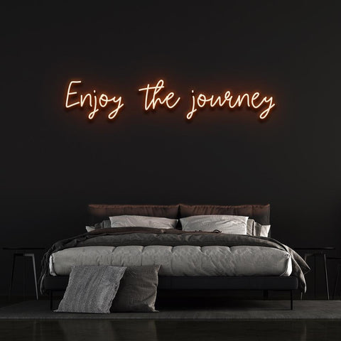 Enjoy the Journey neon sign in orange color, creating a calm and modern look for bedroom walls.