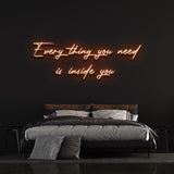 Everything you need is inside you neon sign in orange, complementing a cozy bedroom environment.