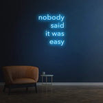 Soft light blue 'Nobody Said It Was Easy' LED neon sign, ideal for home or office motivational decor, reminding you to stay focused and never give up.